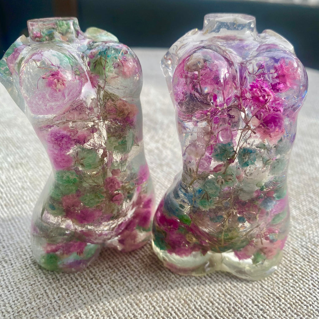 Two clear resin woman torsos filled with pink and green flowers on a textured surface.