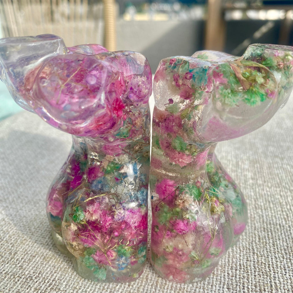 Two mini glass like woman torsos filled with colorful pink blue and green flowers